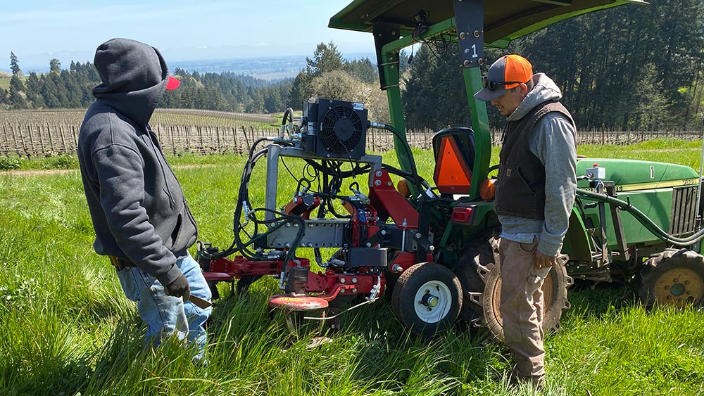 photo of two men looking at a tractor in the vineyard