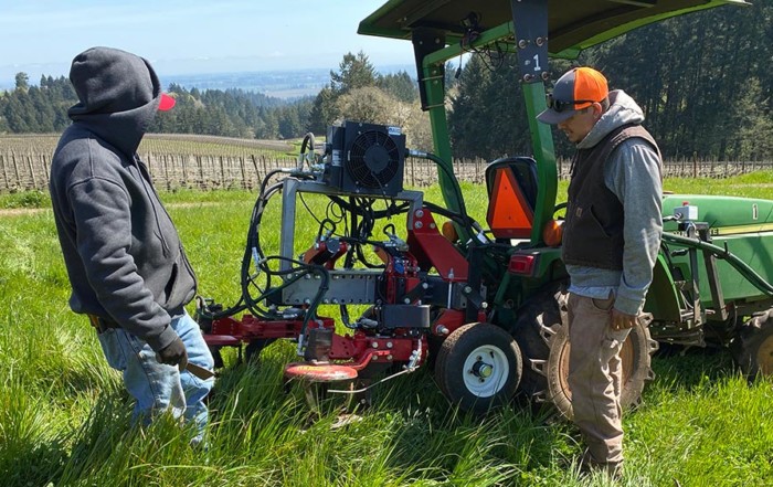 photo of two men looking at a tractor in the vineyard