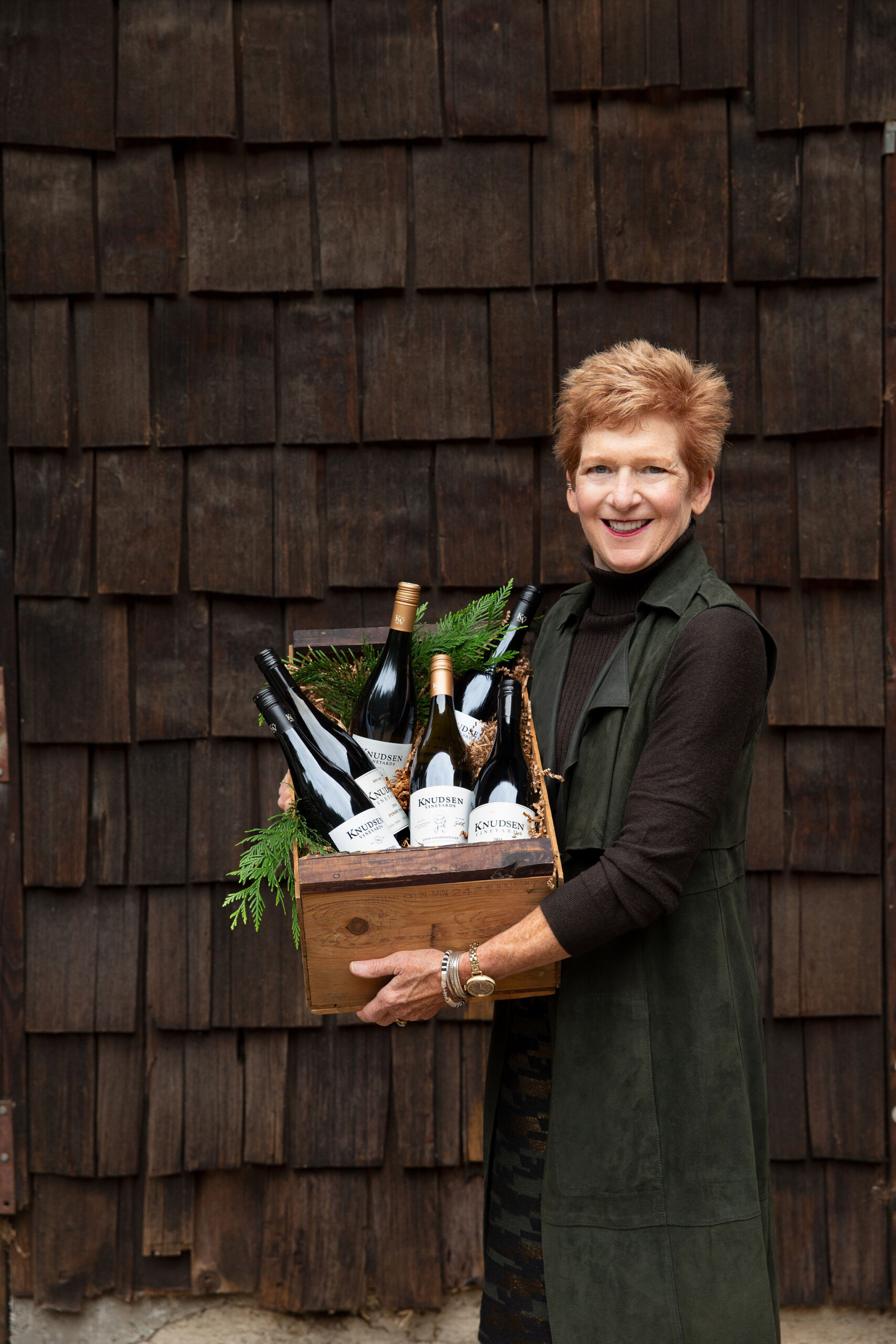 Photo of a smiling woman holding a festive crate with 6 bottles of wine.