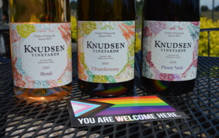 The Knudsen Vineyards Family Series lined up with a pride sticker that says "you are welcome here"